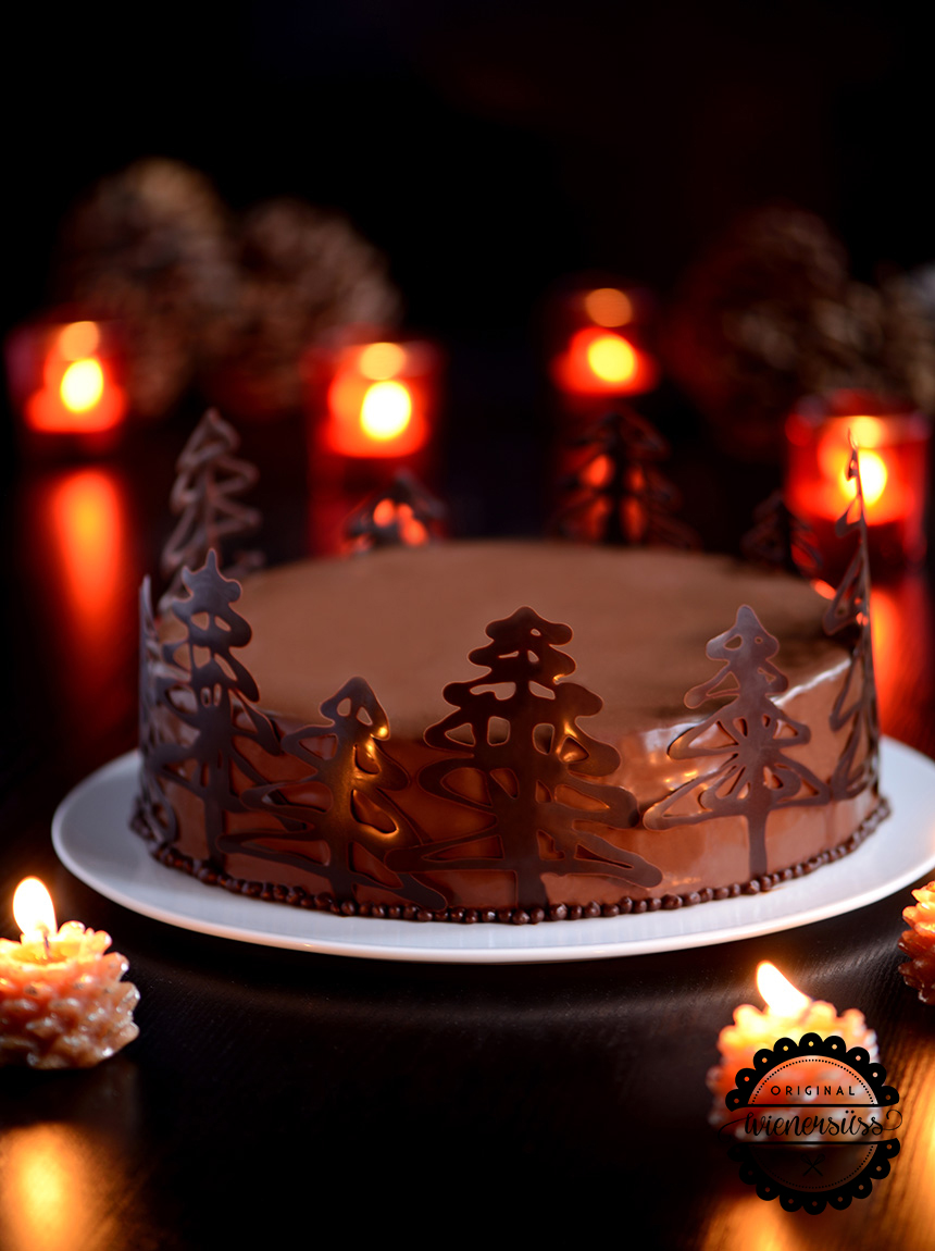 Die Schokoladenmousse-Torte mit Maracujacreme ist mit einer glänzenden Schokoladenglasur überdeckt und weihnachtlich dekoriert. Denn um den Rand der Torte ranken sich kleine Tannenbäumchen aus aufgespritzter Schokolade.