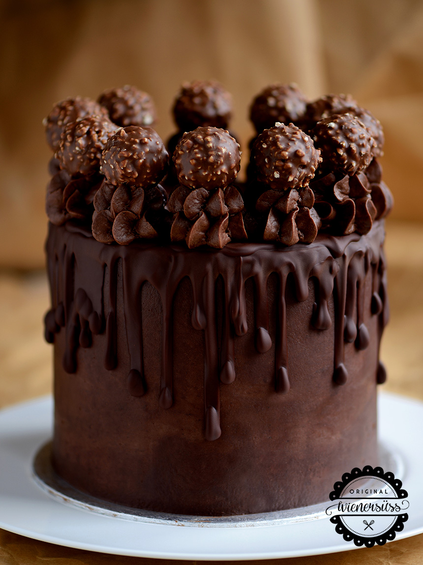 DIe Nutella Ferrero Rocher Torte ist mit Schokolade ummantelt. Seitlich rinnen die Schokoladentröpfchen der Glasur runter und oben ist die Torte mit Ferrero Rocher dekoriert, die auf hohen Schokotuffs einen Platz finden.